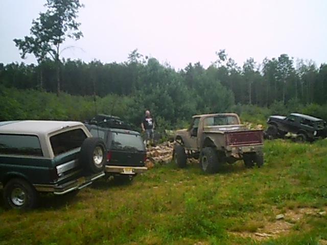 Several off-road vehicles parked on grass with trees in the background. One truck is in the foreground