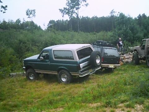 1988 Ford Bronco - A green Ford Bronco with a spare tire on the back is parked in a grassy area with other vehicles.