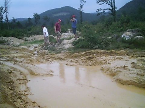 1988 Ford Bronco - Off-road terrain with puddles and people walking. The scene is hilly and wooded.