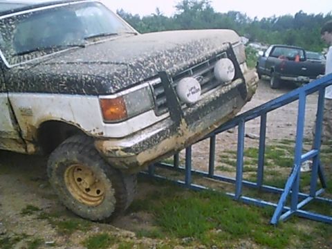 1988 Ford Bronco - A muddy Ford F-Series truck is positioned on a blue ramp during an off-road event.
