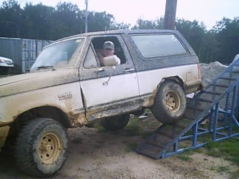 1988 Ford Bronco - Mud-covered 1988 Ford Bronco ascends a ramp during an off-road event.