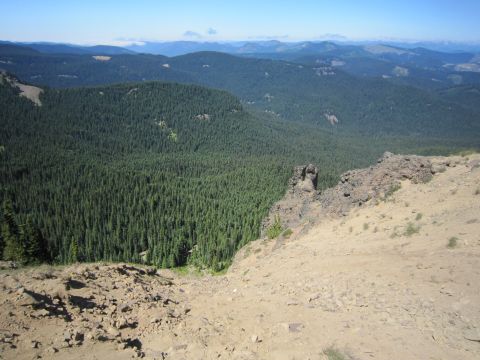 2008 Jeep Wrangler - A vast expanse of evergreen forest stretches across rolling hills, with a rocky outcrop in the foreground under a bright blue sky.
