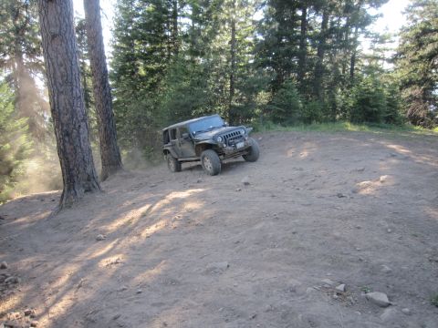 2008 Jeep Wrangler - A Jeep Wrangler navigates a dusty, wooded trail, kicking up dirt as it ascends a slope.
