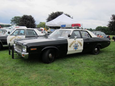1991 Ford LTD Crown Victoria - Black-and-white Highway Patrol sedan with gold door shield, push bumper and light bar, front three-quarter view on grass.