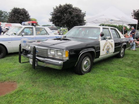 1991 Ford LTD Crown Victoria - Black-and-white Highway Patrol sedan with gold door shield and push bumper, front three-quarter view on grass at a show.