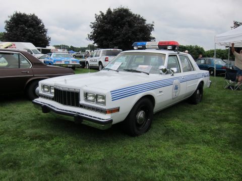 1991 Ford LTD Crown Victoria - White police sedan with blue striping, door emblem and light bar, front three-quarter view parked on grass at a car show.
