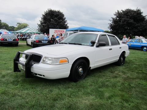 1991 Ford LTD Crown Victoria - Plain white Ford Crown Victoria police sedan with front push bumper parked on grass among other cruisers at a show.