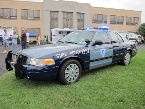 1991 Ford LTD Crown Victoria - two-tone blue State Police Ford Crown Victoria numbered 1257 with a light bar is parked on grass before a brick building.