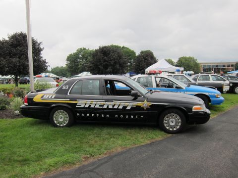 1991 Ford LTD Crown Victoria - Profile of a black Hampden County Sheriff Ford Crown Victoria with gold 911 striping parked beside a paved path at a show.