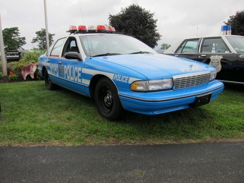 1991 Ford LTD Crown Victoria - light blue NYPD-marked Chevrolet Caprice sedan with a roof light bar is parked on grass at an outdoor vehicle gathering.