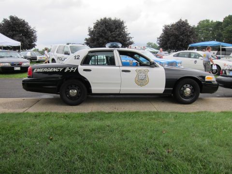 1991 Ford LTD Crown Victoria - Side view of a black-and-white police Crown Victoria numbered 12 marked Emergency 9-1-1 with gold badge decal at a show.