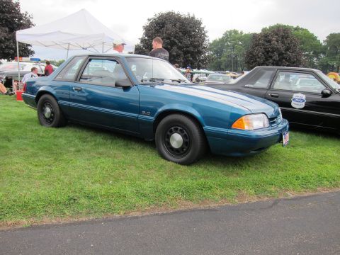 1991 Ford LTD Crown Victoria - teal Fox-body Ford Mustang two-door coupe on black steel wheels is parked on grass at an outdoor car show.