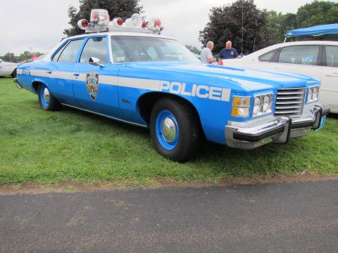 1991 Ford LTD Crown Victoria - light blue 1970s NYPD-marked Pontiac police sedan with roof beacons and chrome bumper sits on grass at a vehicle show.