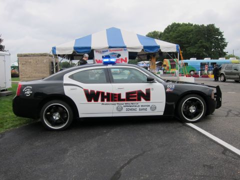 1991 Ford LTD Crown Victoria - Profile view of a black-and-white Dodge Charger sedan with large Whelen graphics parked in front of a tent at an outdoor show.