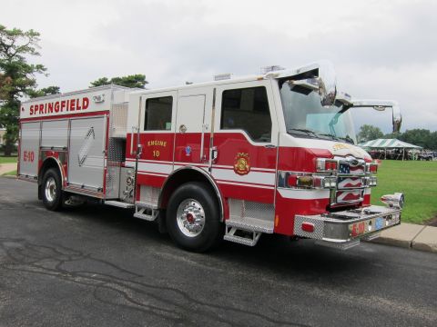 1991 Ford LTD Crown Victoria - Front three-quarter view of a red-and-silver Springfield Engine 10 fire engine parked on a lot with trees and tents behind.