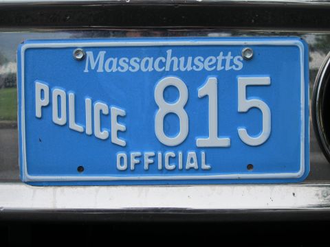 1991 Ford LTD Crown Victoria - Angled close-up of a blue Massachusetts POLICE OFFICIAL license plate reading 815 on a chrome bumper.