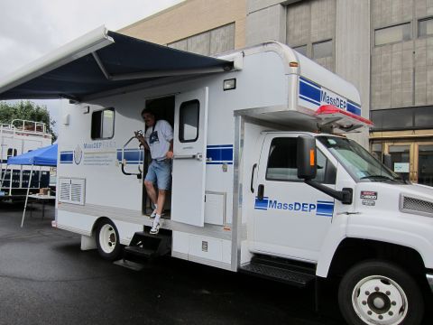 1991 Ford LTD Crown Victoria - white MassDEP mobile response truck with an extended awning and a man standing in the open doorway at an outdoor event.