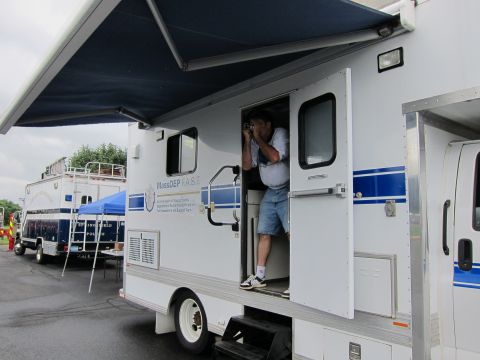 1991 Ford LTD Crown Victoria - man holding a camera stands in the doorway of a white MassDEP mobile truck with a blue awning extended overhead.