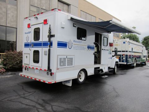 1991 Ford LTD Crown Victoria - Rear three-quarter view of a white-and-blue MassDEP mobile response truck parked beside a command vehicle near a building.