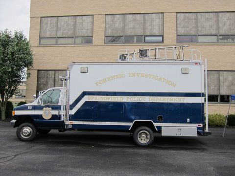 1991 Ford LTD Crown Victoria - Profile view of a blue-and-white Springfield Police Department Forensic Investigation box truck parked on a lot by a brick building.