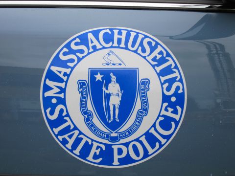 1991 Ford LTD Crown Victoria - Close-up of a blue-and-silver Massachusetts State Police seal decal on the dark glossy body panel of a patrol car.