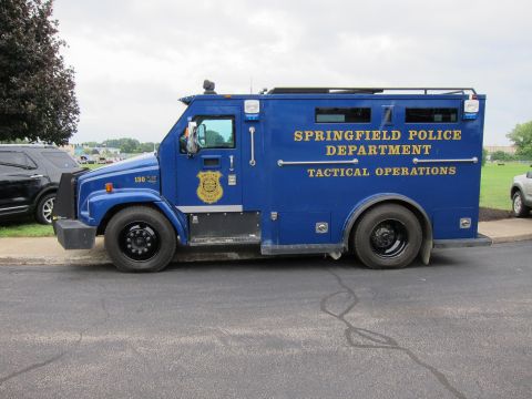 1991 Ford LTD Crown Victoria - Blue Springfield Police Department 'Tactical Operations' armored truck viewed from the side, parked beside other vehicles.