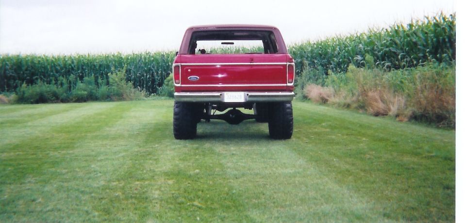Rear of a lifted red two-door Bronco on big tires parked on mowed grass beside a cornfield