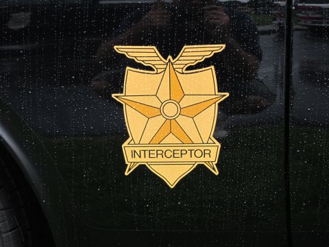 1991 Ford LTD Crown Victoria - Close-up of a gold winged-star 'INTERCEPTOR' decal applied to the rain-beaded black door of a car.