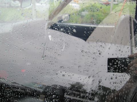 1991 Ford LTD Crown Victoria - car's side window covered in rain droplets, the pale interior seats faintly visible through the wet glass.
