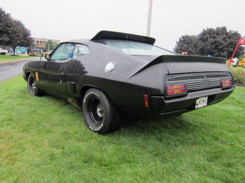 1991 Ford LTD Crown Victoria - Rear three-quarter view of a black customized fastback muscle car with white-letter tires parked on a grassy show field.