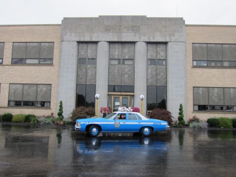 1991 Ford LTD Crown Victoria - blue police sedan parked on wet pavement in front of a building whose facade reads 'Smith & Wesson'.