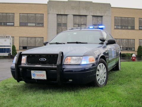1991 Ford LTD Crown Victoria - Front three-quarter view of a dark blue Ford Crown Victoria State Police cruiser with push bar, lit roof bar and 'TROOPER' plate.