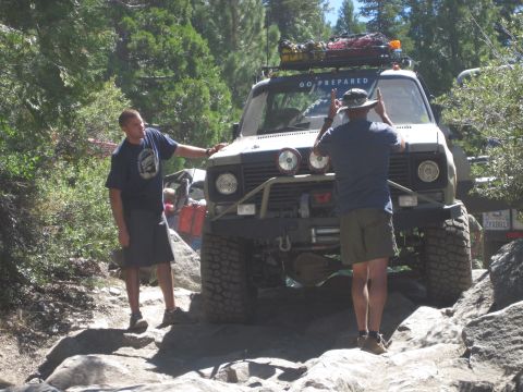 1989 Ford Bronco - Two men guide an off-road vehicle over a challenging rocky trail, with another vehicle visible in the background.