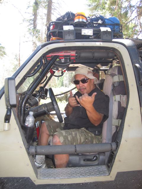 1989 Ford Bronco - Man in a modified off-road vehicle gives a shaka sign while sitting in the driver's seat.