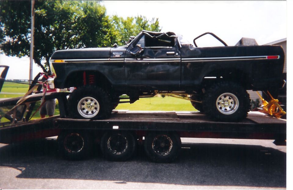Black lifted Ford Bronco with collapsed top loaded on a triple-axle flatbed trailer, side view