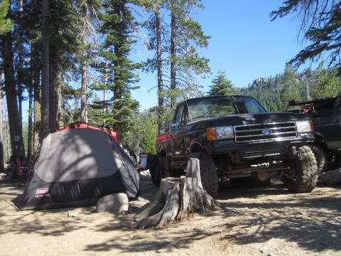 1989 Ford Bronco - A black Ford pickup truck is parked at a campsite next to a tent, with a mountainous forest in the background.