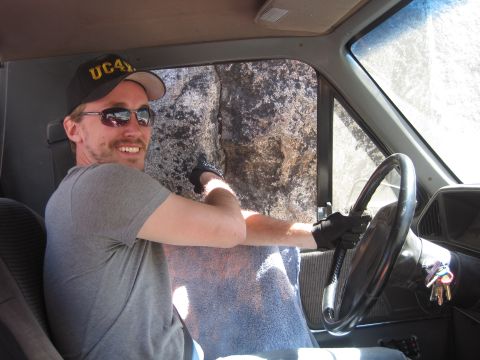 1989 Ford Bronco - Driver in a truck navigates a rocky, off-road path, with a large boulder visible through the passenger window.
