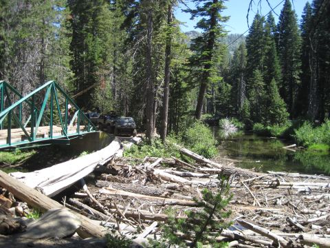 1989 Ford Bronco - Several off-road vehicles are seen navigating a wooded area with a bridge and a river.