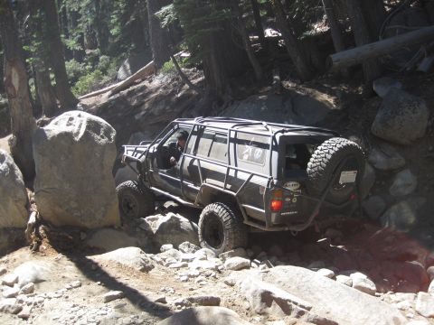 1989 Ford Bronco - An off-road SUV navigates a challenging rocky trail through a forest.