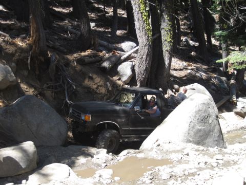 1989 Ford Bronco - Pickup truck maneuvering through a challenging off-road course with large rocks and mud.