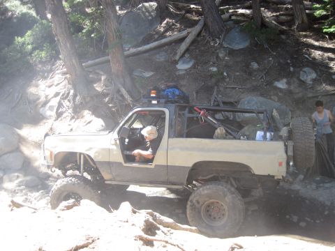 1989 Ford Bronco - This heavily modified SUV is tackling a challenging off-road trail with steep inclines and large rocks.