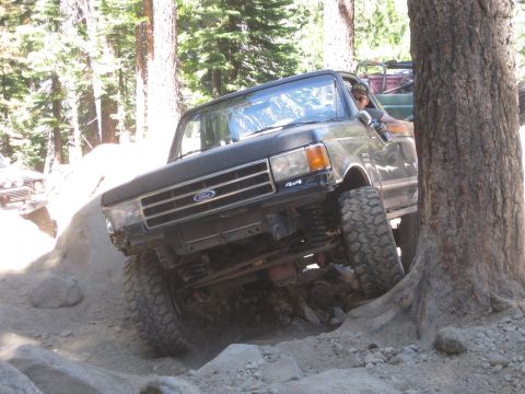 1989 Ford Bronco - A Ford F-Series truck is shown off-roading on a rocky trail, with a second vehicle partially visible behind it.