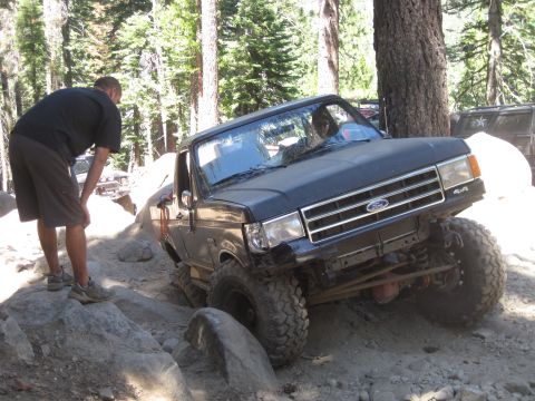 1989 Ford Bronco - A black Ford Bronco navigates a challenging rocky terrain, with a person observing the vehicle's progress.
