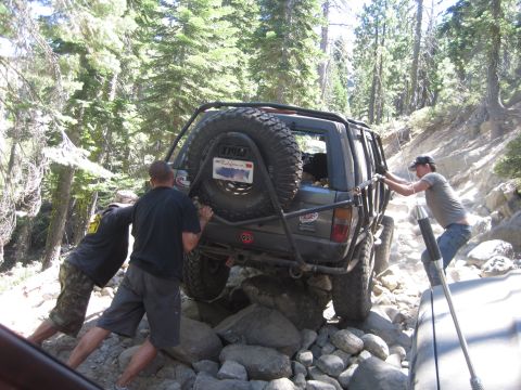 1989 Ford Bronco - People push an off-road SUV stuck on a rocky trail, with another vehicle nearby.