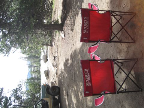1989 Ford Bronco - Camping chairs and an off-road vehicle are parked on a dirt area with trees and rocks.