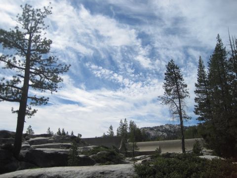 1989 Ford Bronco - A scenic view of a rocky terrain with scattered trees and a large dam structure against a dramatic sky.