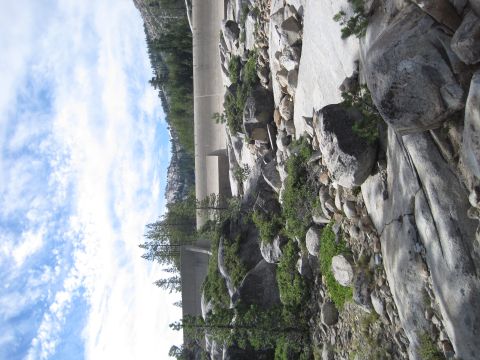 1989 Ford Bronco - A large concrete dam is visible behind a rocky slope with trees under a cloudy sky.