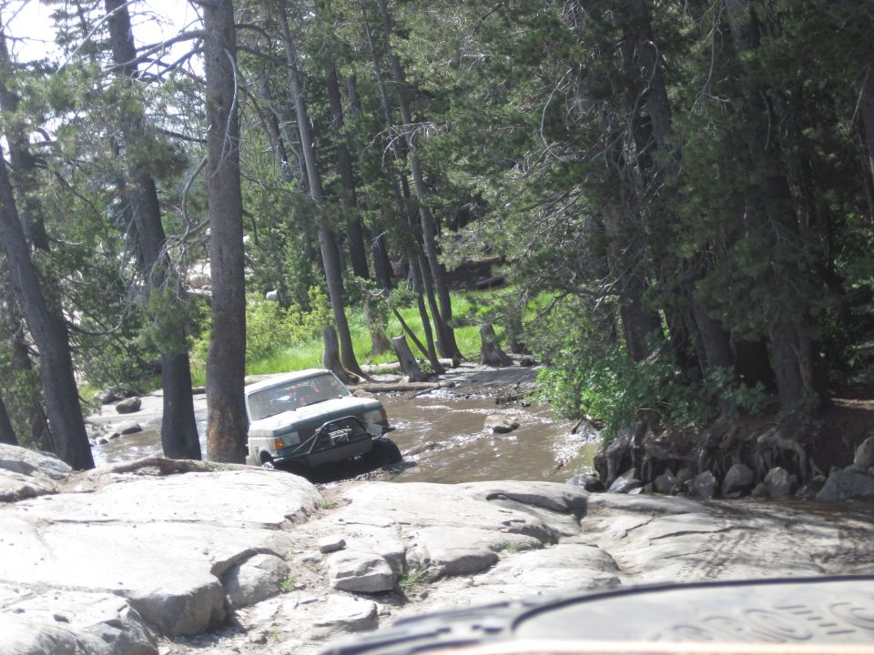 off-road vehicle driving through shallow water and mud in a wooded area