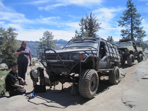 1989 Ford Bronco - Two off-road vehicles are on a rocky trail, with people attending to the front vehicle.