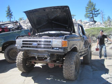 1989 Ford Bronco - A black Ford truck, likely from the late 1980s, sits with its hood open next to another vehicle in a rocky, outdoor setting.